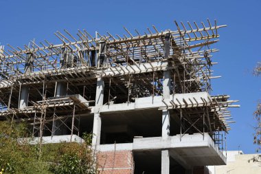 Bina inşaatın ilk aşamalarında, mavi gökyüzü arka planında. Tahta iskeleler yeni yapıların beton kirişlerini ve sütunlarını ortaya çıkardı. Şehir sokağı, devam ediyor. Atina, Yunanistan.