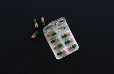 Kabarcıktaki kapsül hapları, siyah arka planda yakın plan. Bir paket hap açtım. İçinde çok renkli granüller olan jelatin kapsüller. İlaç, oral uyuşturucu. Vitaminler, takviyeler. Eczane, sağlık hizmetleri.