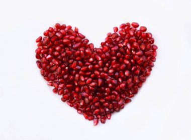 Beyaz zemin üzerinde kalp şeklinde nar tohumları, parlak granatum çekirdekleri güzel kırmızı tonlarını gösteriyor. Yarı şeffaf, sulu olgun meyveler, taze sağlıklı gıda konsepti..