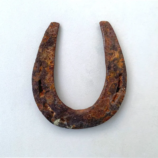 Old rusty metal horseshoe isolated on white background, top view. Used classic steel horseshoe, badly worn, aged surface is pitted by heavy rust. Antique or vintage talisman, a symbol of good luck.