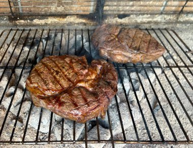 Et, odun yakan bir ızgarada pişiriliyor, yakın plan. Taze ekmek dilimleriyle servis edilen lezzetli bir et parçası. Piknik yemekleri