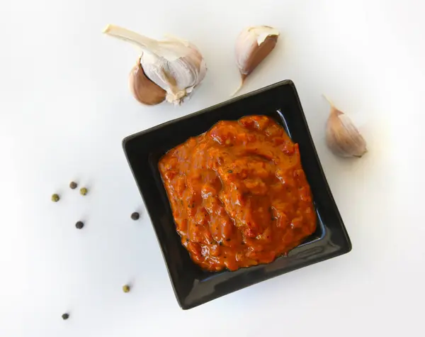 Bowl of red sauce, close-up,garlic on a white background. Homemade sauce, seasoning,spicy paste. Bulgarian lutenitsa, aur Balkan ajvar, with tomatoes, eggplants, paprika, garlic. Traditional seasoning