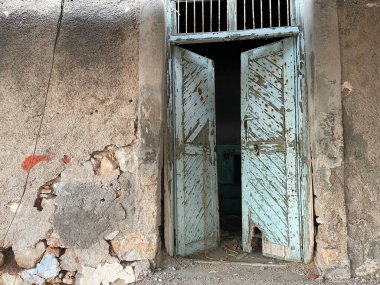 Eski Akdeniz evi dış duvarı, açık ahşap kapılar. Çatlamış cepheli terk edilmiş bir bina, eski parçalanmış alçıdan yapılmış tuğlalar. Atina, Yunanistan.