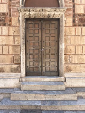 Giriş kapısı olan eski bir binanın ön cephesi. Çifte ahşap kapılar. Yunanistan 'ın başkenti Atina' da güneşli bir sokağa çıkan mermer basamaklı kilise girişi.