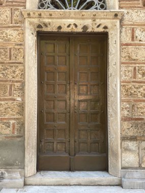 Giriş kapısı olan eski bir binanın ön cephesi. Çifte ahşap kapılar. Yunanistan 'ın başkenti Atina' da güneşli bir sokağa çıkan mermer basamaklı kilise girişi.