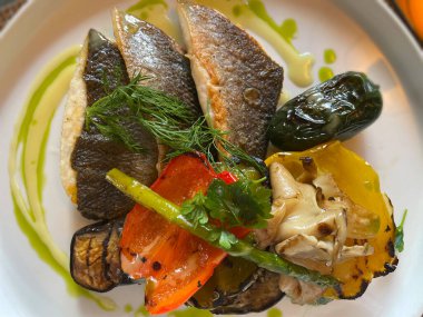 Restoran masasında kızarmış balık. Izgara sebze. Biber, patlıcan, kabak ve kuşkonmaz. Güzel bir yemek sunumu. Vejetaryenler için sağlıklı yiyecekler..