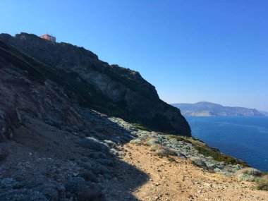 Ormanlık dağ sıraları ve deniz manzarası. Geniş bulutlu bir gökyüzünün altında, vadideki bir köyün üzerinde bir tutam beyaz sis bulunan yeşil tepeler. Yunanistan.