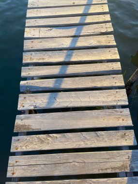 Arkasında deniz olan ahşap bir patika. Suyun üzerinde ahşap kalaslar olan kırsal bir yol. Yakın plan. Ahşap zemin tekneye ulaşmamıza yardımcı olur..