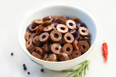 Beyaz bir kasede dilimlenmiş Kalamata zeytinleri. Zeytinyağı, bitki ve baharatla marine edilmiş Yunan zeytinleri. Akdeniz aperatifi, sağlıklı vejetaryen aperatifi ve yemek ve salata malzemesi..