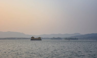 Gün batımında sakin denizde, dağların arkasında Çin usulü bir turist teknesi. Bulut yok. Seyahat, geçmiş ve blog gibi şeyler için. Kavramları. Batı Gölü. Hangzhou şehrinin popüler parkı.