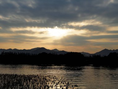 Gün batımında dağları olan sakin bir deniz manzarası. Dramatik gökyüzü ve bulut manzarası. Seyahat, geçmiş ve blog gibi şeyler için. Kavramları. Batı Gölü. Hangzhou şehrinin popüler parkı.