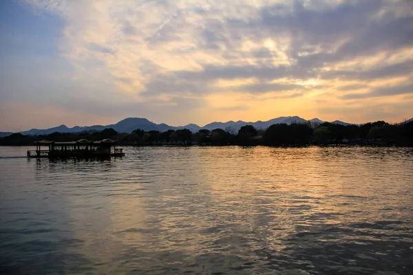 夕阳西下 一艘船和一个人在平静的海面上航行 背景是群山和太阳光 戏剧化的天空和云彩 博客等 西湖杭州人民公园中国 — 图库照片