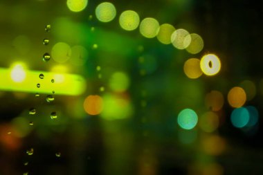Gece sokak ışıklarının yeşil ve sarı renkli Bokeh etkisi. Önplan olarak da yağmur damlalarının odağı. Araba penceresinden bakıyorum..
