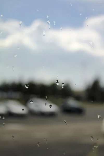 Close-up of the raindrops on car window with blurred cloud and blue sky in the background.