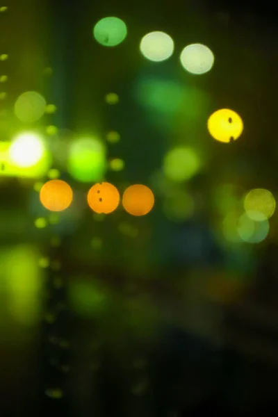 Bokeh effect of street lighting at night in green and yellow color with the focus of some raindrops as foreground. Looking through from car window.