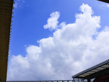 Binadan gökyüzünün alt görüntüsü. Çatı açılıyor. Mavi gökyüzü ve beyaz kabarık bulutlar.