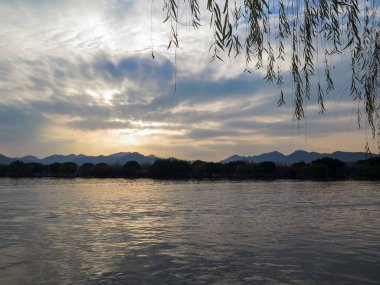 Gün batımında dağları olan sakin bir deniz manzarası. Dramatik gökyüzü ve bulut manzarası. Seyahat, geçmiş ve blog gibi şeyler için. Kavramları. Batı Gölü. Hangzhou şehrinin popüler parkı.
