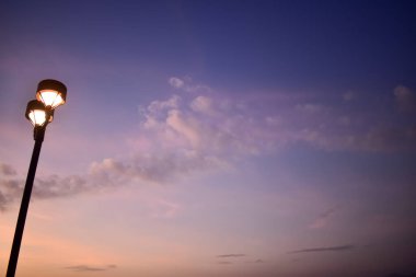 Gün batımında sokak lambasına yakın çekim, arka planda gökyüzü olan şehir ışığı. Şehir manzarası ve şehir merkezi.