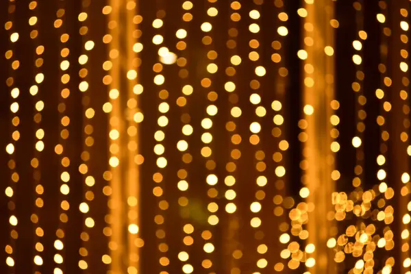 Abstract bokeh effect of the gold, yellow lights on black background. City street light decorations. Rows of LED gold colored light spots with black background.