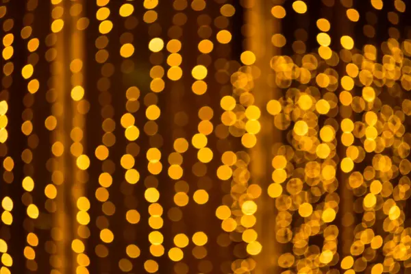 Abstract bokeh effect of the gold, yellow lights on black background. City street light decorations. Rows of LED gold colored light spots with black background.