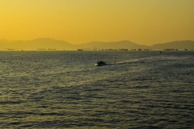 Günbatımında deniz manzarası, arka planda gemiler ve şehir manzarası. Güneş ışınları sakin denizi yansıtıyor. Deniz arka planı ve şehir manzarası. Doğa konsepti.