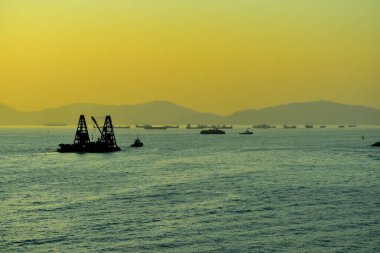 Günbatımında deniz manzarası, arka planda gemiler ve şehir manzarası. Güneş ışınları sakin denizi yansıtıyor. Deniz arka planı ve şehir manzarası. Doğa konsepti.