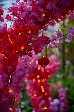 Close-up of the Chinese traditional red lantern decor with artificial peach blossom flower in outdoors. Festive decoration and celebration. Chinese New Year decoration. For background use. clipart