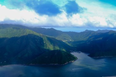 Bulutlu manzaralı uçak penceresinden bakıyorum. Hong Kong dağlarının üzerinde mavi gökyüzü olan tüylü beyaz bulutlar. Hong Kong kırsal alanı, yüksek açılı manzaralı dağlar. Doğa sahnesi.