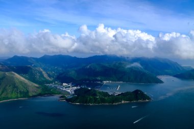 Bulutlu manzaralı uçak penceresinden bakıyorum. Hong Kong dağlarının üzerinde mavi gökyüzü olan tüylü beyaz bulutlar. Hong Kong kırsal alanı, yüksek açılı manzaralı dağlar. Doğa sahnesi.