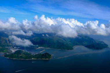 Bulutlu manzaralı uçak penceresinden bakıyorum. Hong Kong dağlarının üzerinde mavi gökyüzü olan tüylü beyaz bulutlar. Hong Kong kırsal alanı, yüksek açılı manzaralı dağlar. Doğa sahnesi.