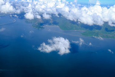 Bulutlu manzaralı uçak penceresinden bakıyorum. Hong Kong dağlarının üzerinde mavi gökyüzü olan tüylü beyaz bulutlar. Hong Kong kırsal alanı, yüksek açılı manzaralı dağlar. Doğa sahnesi.
