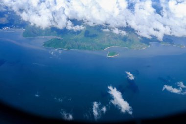 Bulutlu manzaralı uçak penceresinden bakıyorum. Hong Kong dağlarının üzerinde mavi gökyüzü olan tüylü beyaz bulutlar. Hong Kong kırsal alanı, yüksek açılı manzaralı dağlar. Doğa sahnesi.