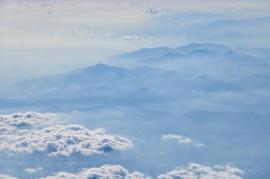 Uçak penceresinden dağların ve bulutların çarpıcı manzarası. Doğal manzaranın havadan görünüşü, dağ sırası. Seyahat ve manzara. Seyahat ve doğa kavramı. 