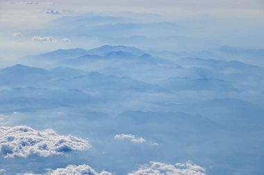Uçak penceresinden dağların ve bulutların çarpıcı manzarası. Doğal manzaranın havadan görünüşü, dağ sırası. Seyahat ve manzara. Seyahat ve doğa kavramı. 