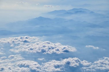 Uçak penceresinden dağların ve bulutların çarpıcı manzarası. Doğal manzaranın havadan görünüşü, dağ sırası. Seyahat ve manzara. Seyahat ve doğa kavramı. 