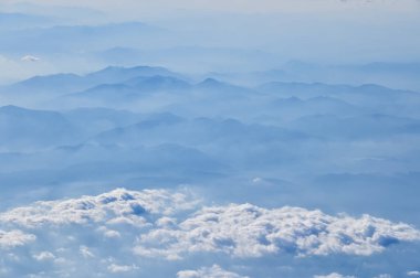 Uçak penceresinden dağların ve bulutların çarpıcı manzarası. Doğal manzaranın havadan görünüşü, dağ sırası. Seyahat ve manzara. Seyahat ve doğa kavramı. 