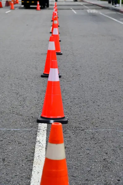 Yoldaki trafik konisine yakın çekim. Parlak turuncu trafik konileri asfaltta sıra sıra bekliyor. Ulaşım aracı, ekipman. Yol çalışıyor. Şehir manzarası.