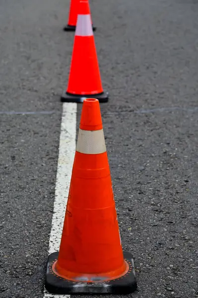Yoldaki trafik konisine yakın çekim. Parlak turuncu trafik konileri asfaltta sıra sıra bekliyor. Ulaşım aracı, ekipman. Yol çalışıyor. Şehir manzarası.