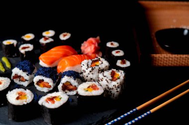 Tabak siyah arkaplanda. Somon, mango, kabak ve spyta souce suşi çubuklarıyla siyah arka planda suşi rulosu..