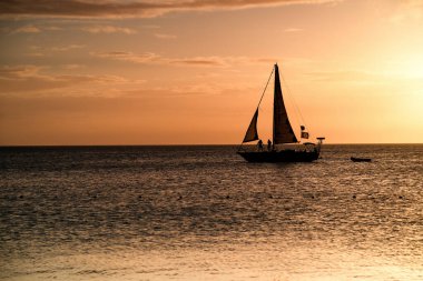 Deniz teknesinde altın saat. Turuncu gün batımında bir yelkenli..