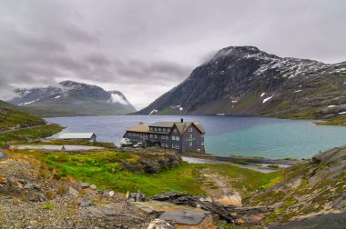 Norveç 'te bir gölün yanında bir otel. Gökyüzünde bulutlar, dağlarda karlar.