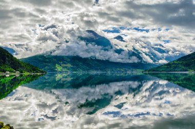 Çok durgun bir su ile güzel bir fiord manzarası ve su ve dağlar üzerindeki bulutların güzel yansımaları.