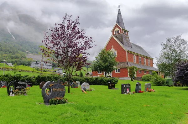 Norveç 'te ahşap bir kilise, yanında mezarlık ve bulutlu yeşil çimenler.