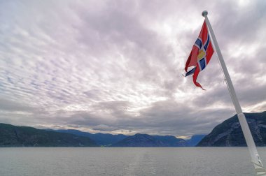 Norveç bayrağı Norveç 'in arka planında bulutlu bir gökyüzü ile bir fiyortta yelken açarken