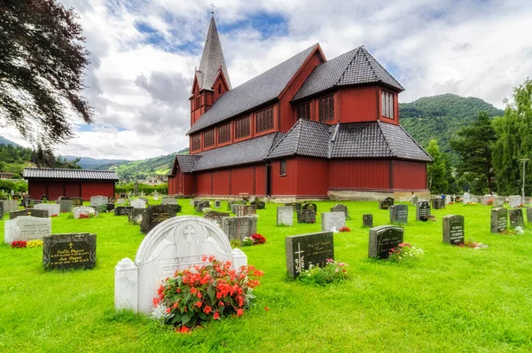 Mezarı kilisenin yanında olan kırmızı ahşap bir kilise ve Norveç 'te bulutlu gökyüzü olan yeşil çimenler.