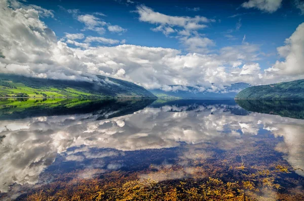 Norveç 'te berrak gökyüzü ve bulutlarla dolu bir fiyortta durgun bir suya yansıyor