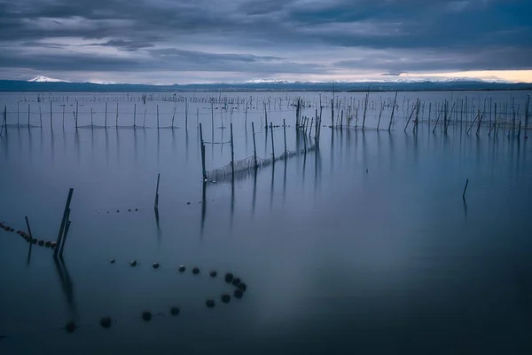 İspanya, Valencia 'daki Albufera gölünde gün batımı. Su üzerinde balık kapanları ve arka planda karla kaplı dağlar.