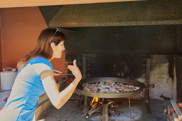 Kız odun ateşiyle geleneksel paella pişiriyor.