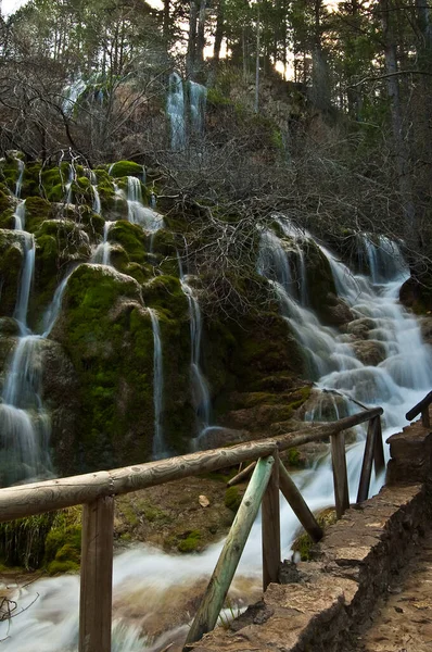 Güzel şelale kayalardan aşağı süzülüyor, şelalenin önünde ahşap bir balyoz var.