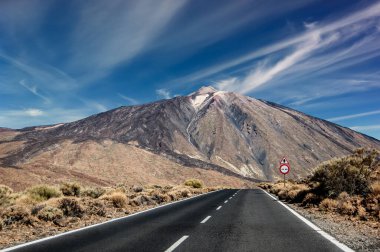 Arka planda Teide volkanı olan ıssız bir yol ve bir çöl manzarasındaki trafik işaretleri aracılığıyla.